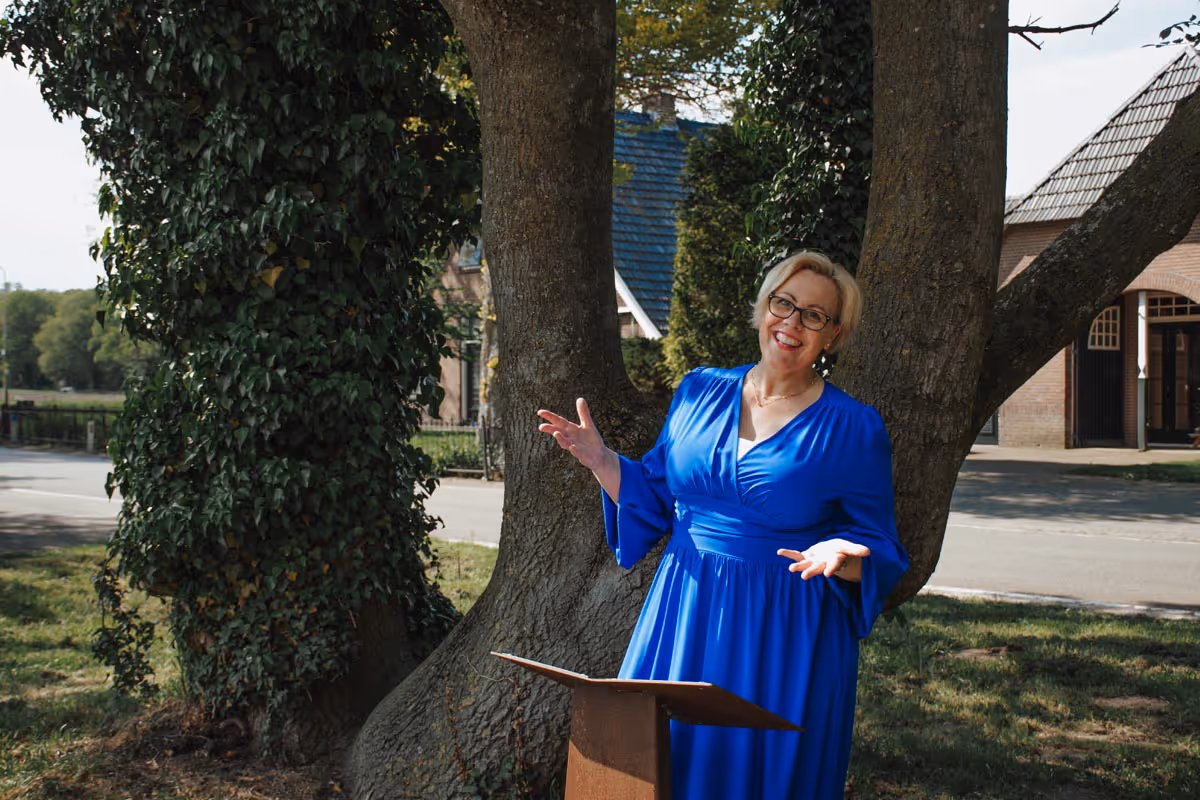 Trouwambtenaar Karin stralend bij een mooi boom staand achhter katheder in een kobalt blauwe jurk
