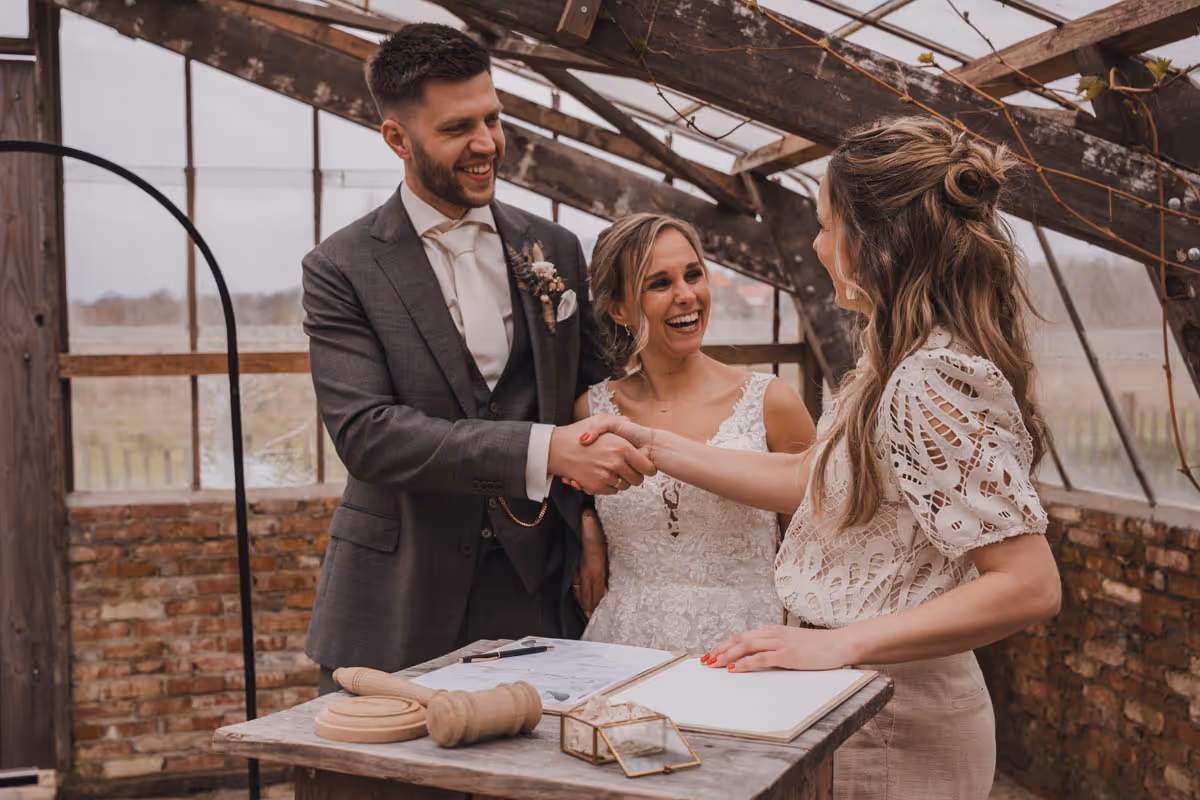 Trouwambtenaar, babs Lisanne van Trouwen met Liefs geeft bruidspaar de hand en felicitataties na de huwelijksvoltrekking
